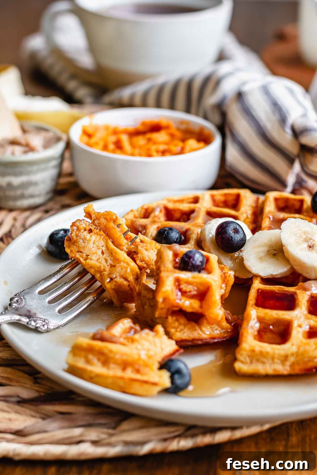 Cut sweet potato waffles on a plate with a fork piercing two pieces.