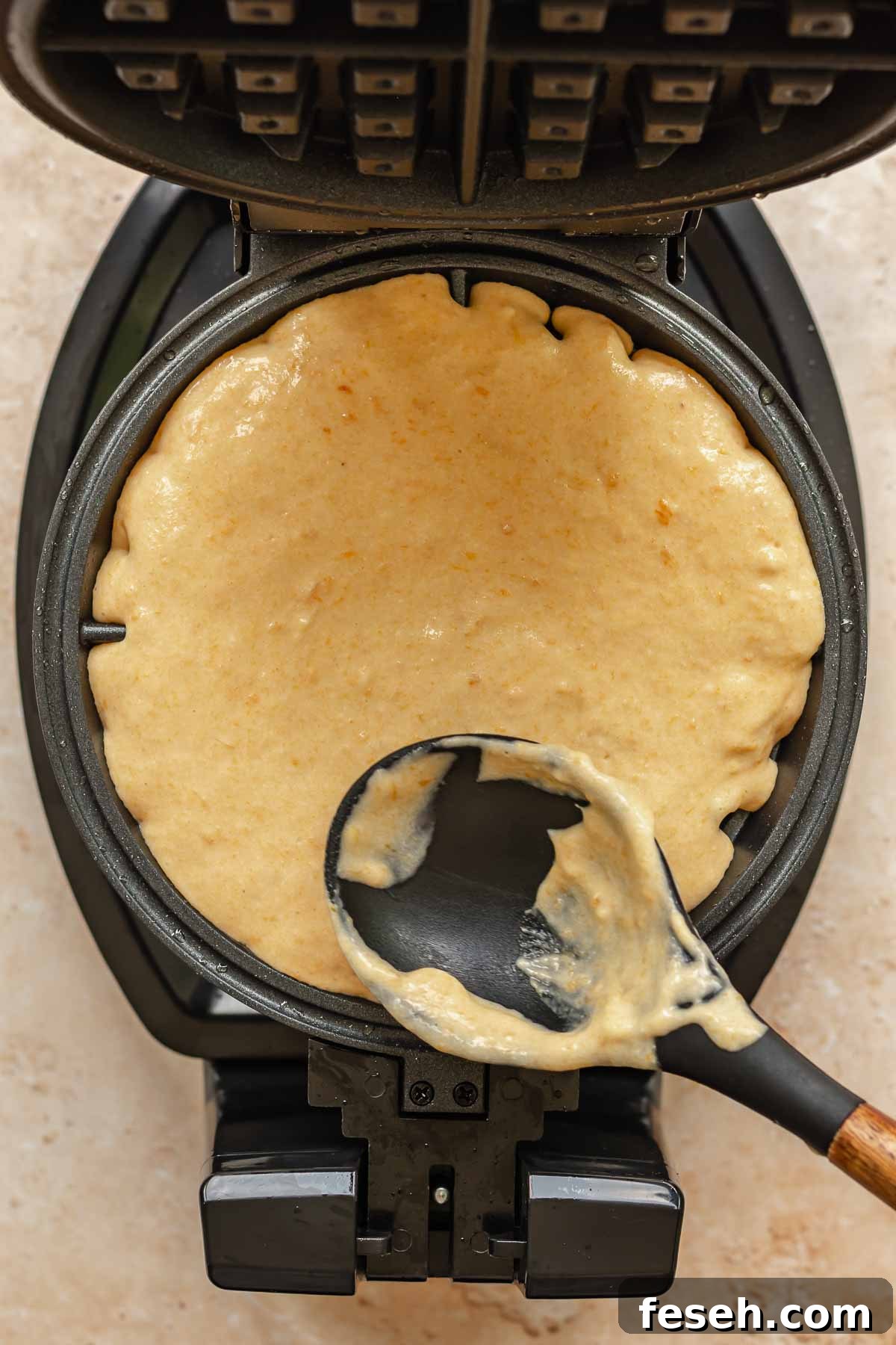 A spoon spreads waffle batter into a waffle iron.