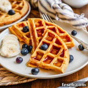 Triangles of sweet potato waffles on a plate with syrup and fruit.