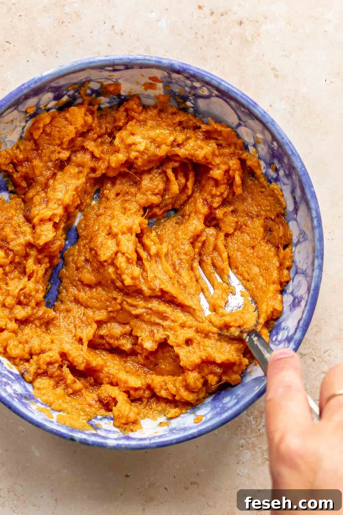 A fork mashes cooked sweet potato in a bowl.