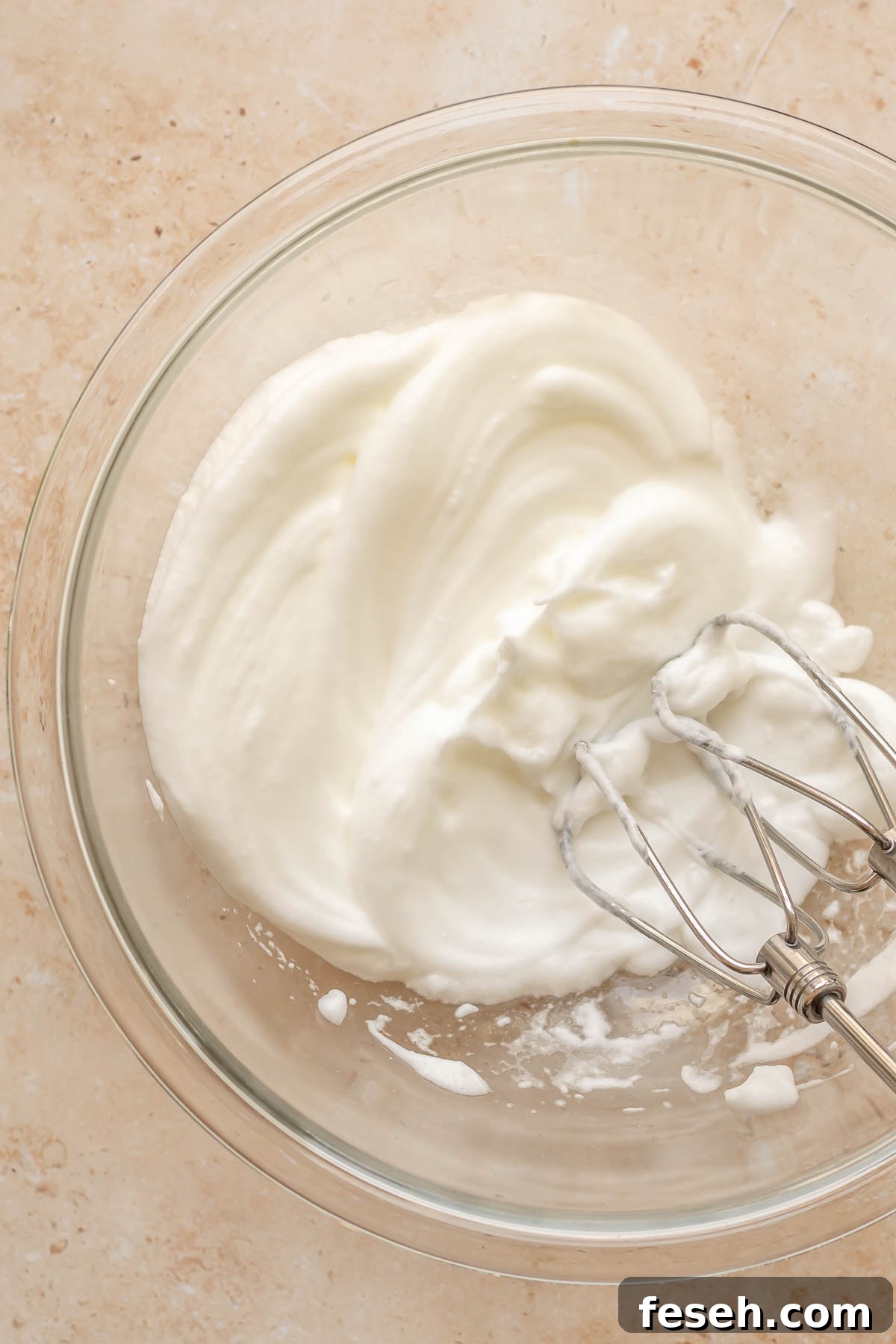 A hand mixes whips egg whites in a bowl.