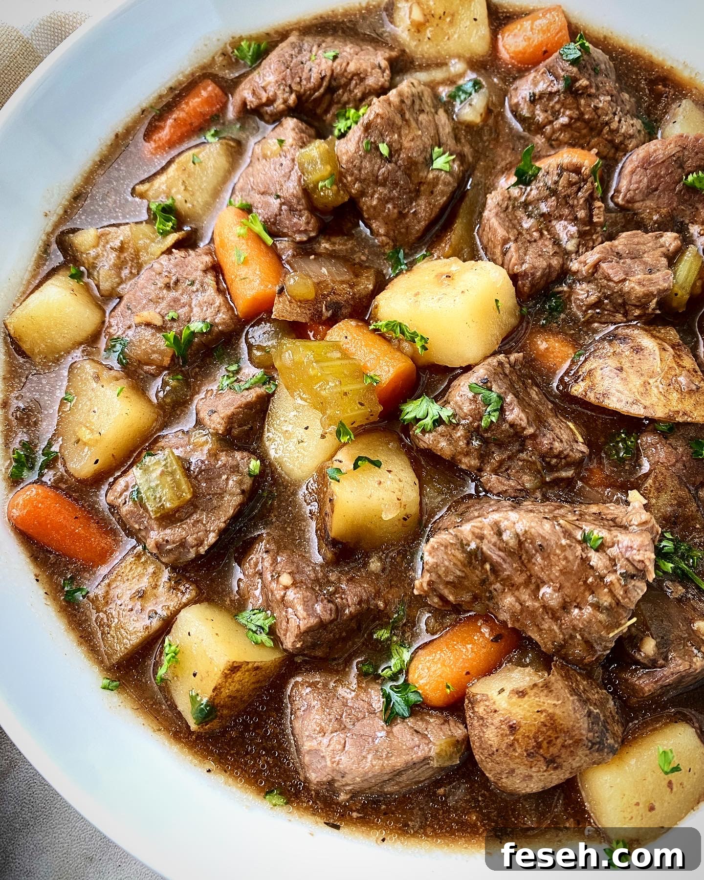 close up shot of cooked Guinness beef stew in a white bowl with a silver spoon
