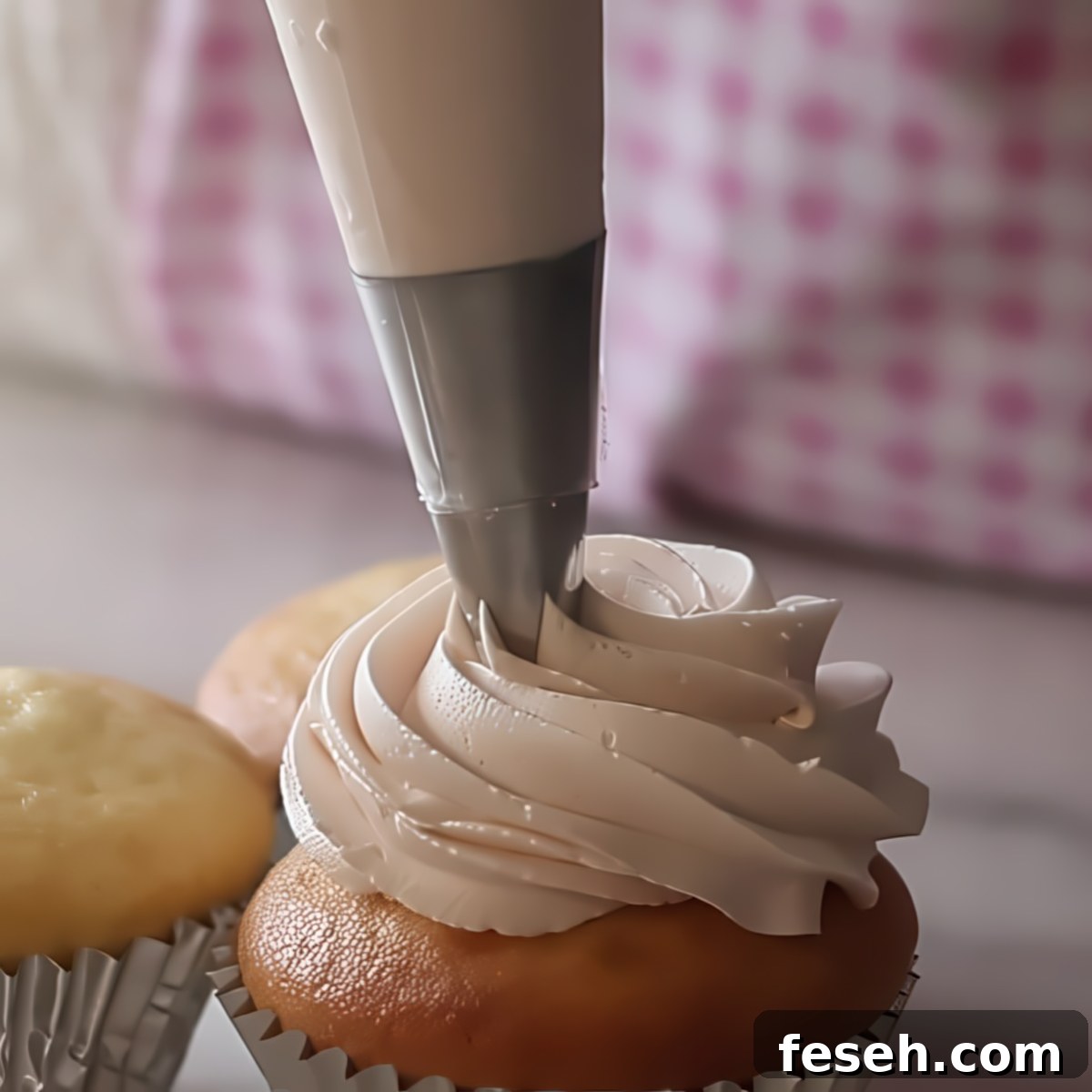 piping light pink buttercream on top of cupcake.