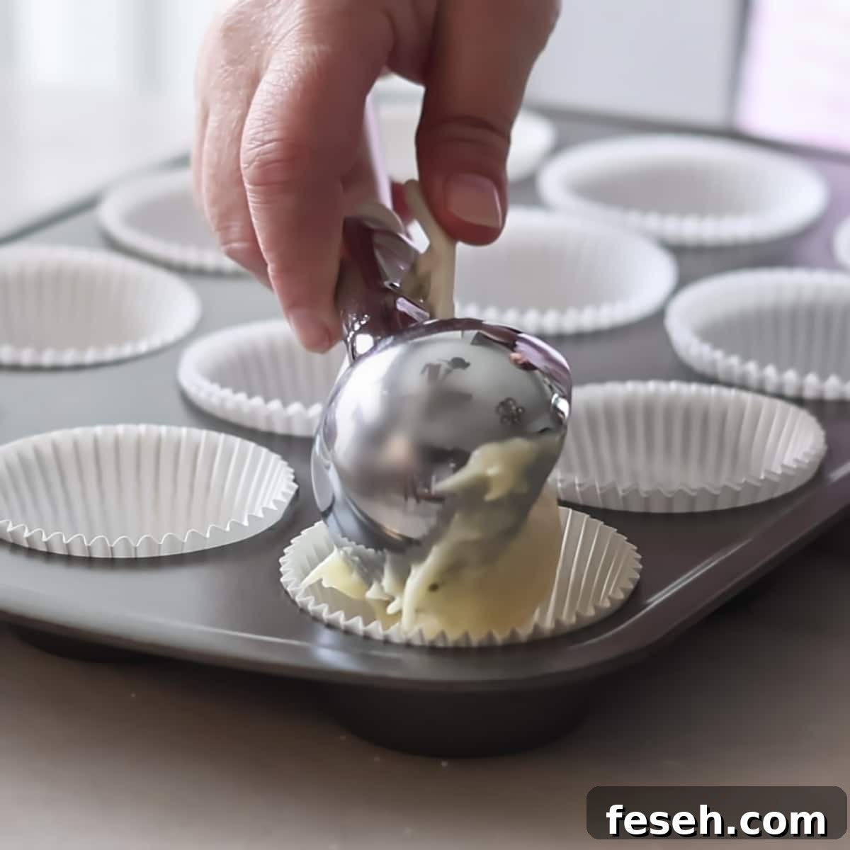 scooping cake batter into cupcake liners in pan.