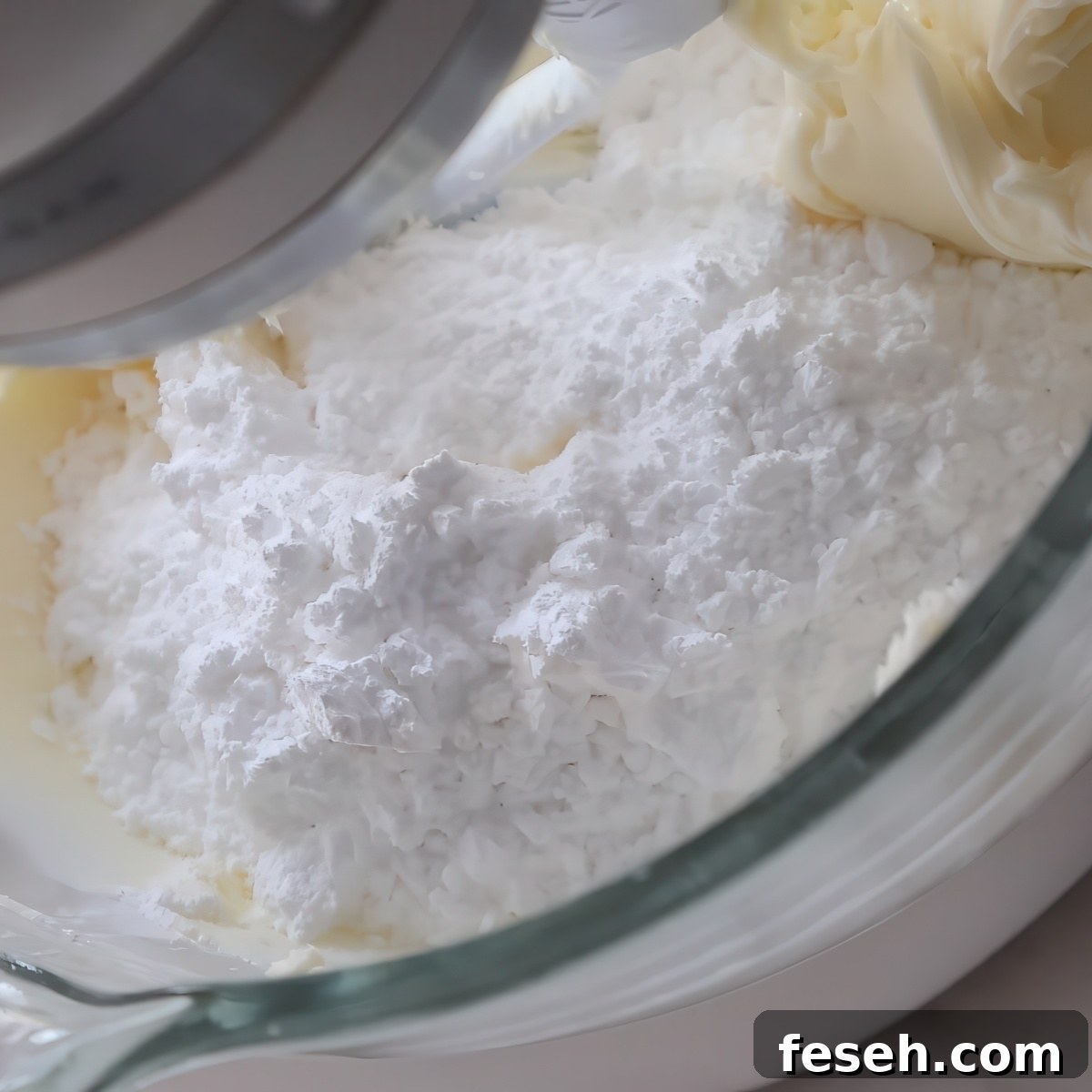 powdered sugar on top of whipped butter in glass stand mixer bowl.