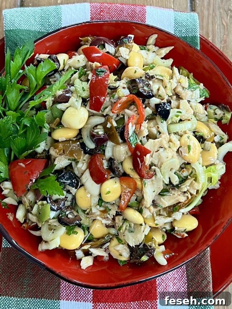 Italian Baccala Salad in red bowl over decorative towel with parsley sprigs garnish.