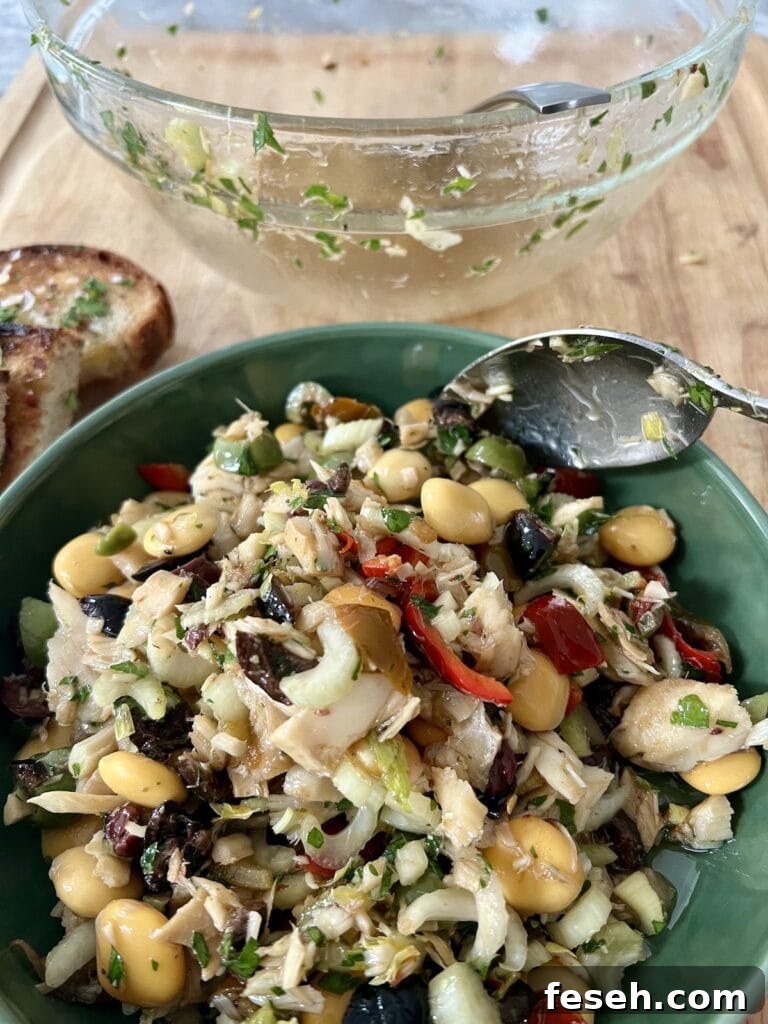 Scooping the salt cod insalata from mixing bowl to green serving bowl with spoon.