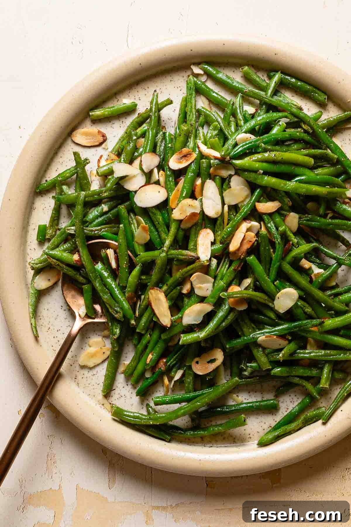 plate of green beans with toasted almonds and spoon resting on the side.