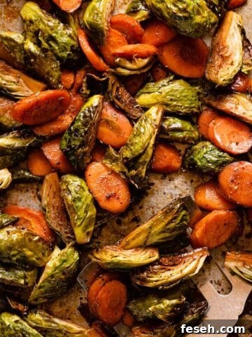 roasted brussels sprouts and sliced carrots on baking pan with spatula on the side