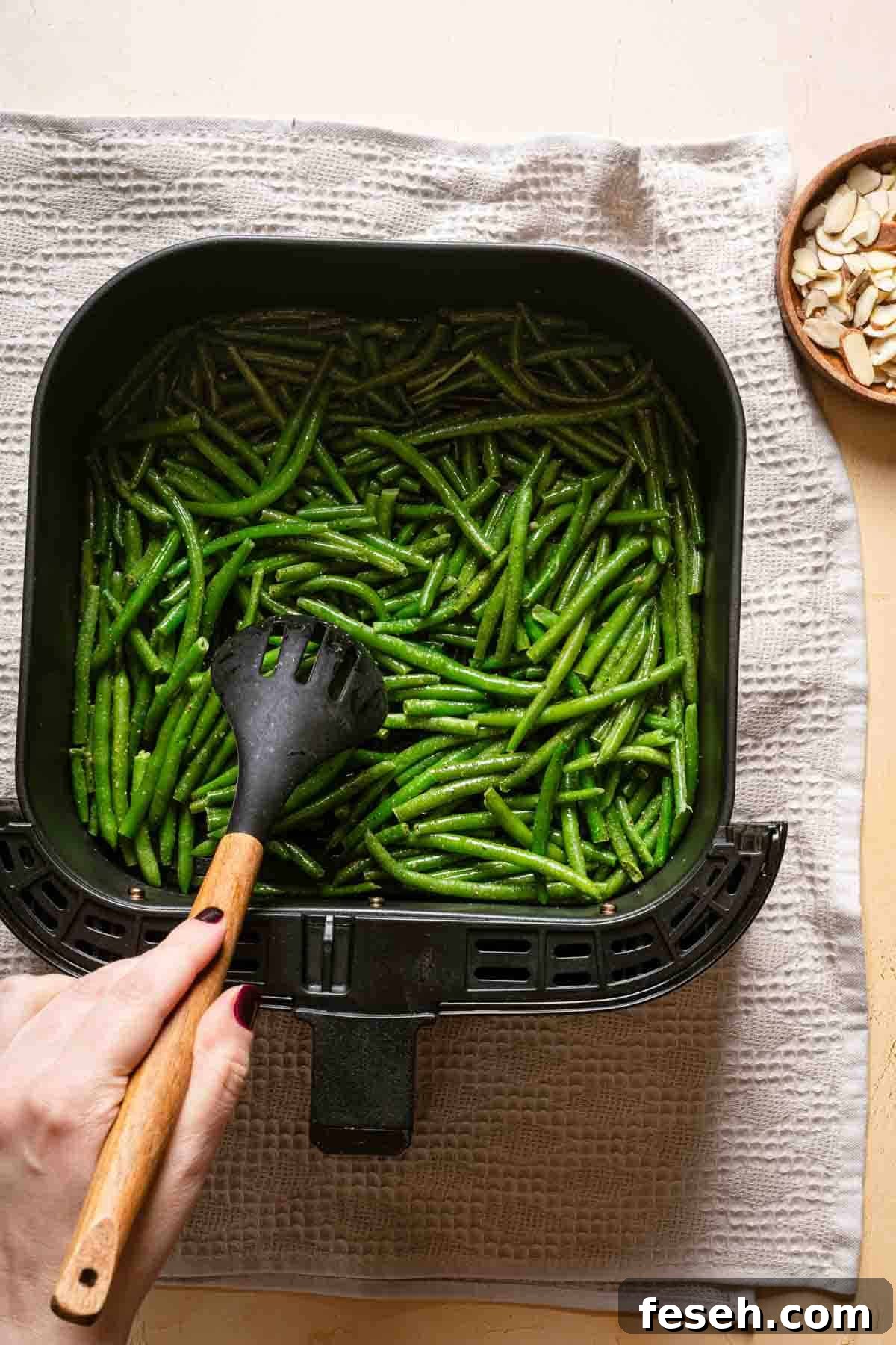 frozen green beans being spread out in air fryer basked with spoon.