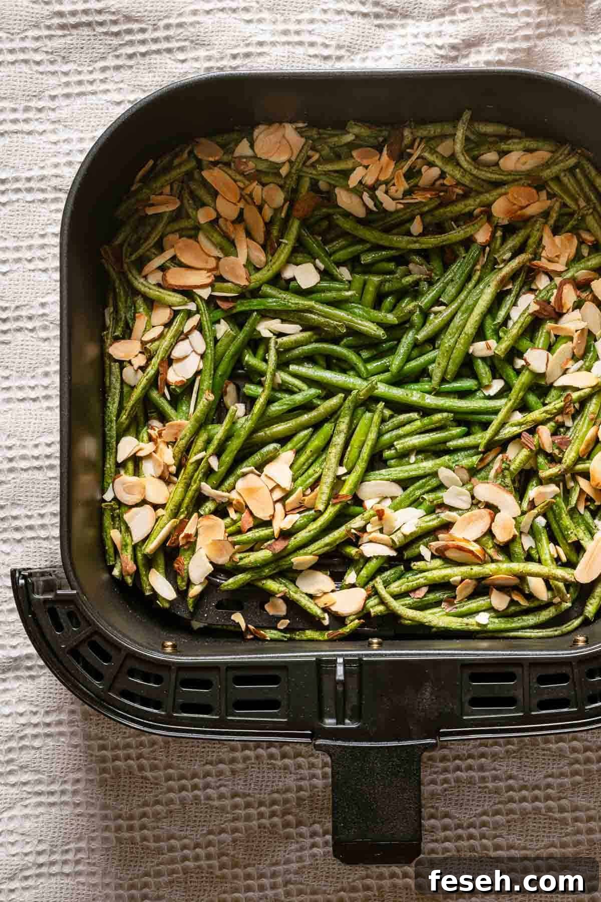 cooked green beans with toasted almonds on top in air fryer basket.