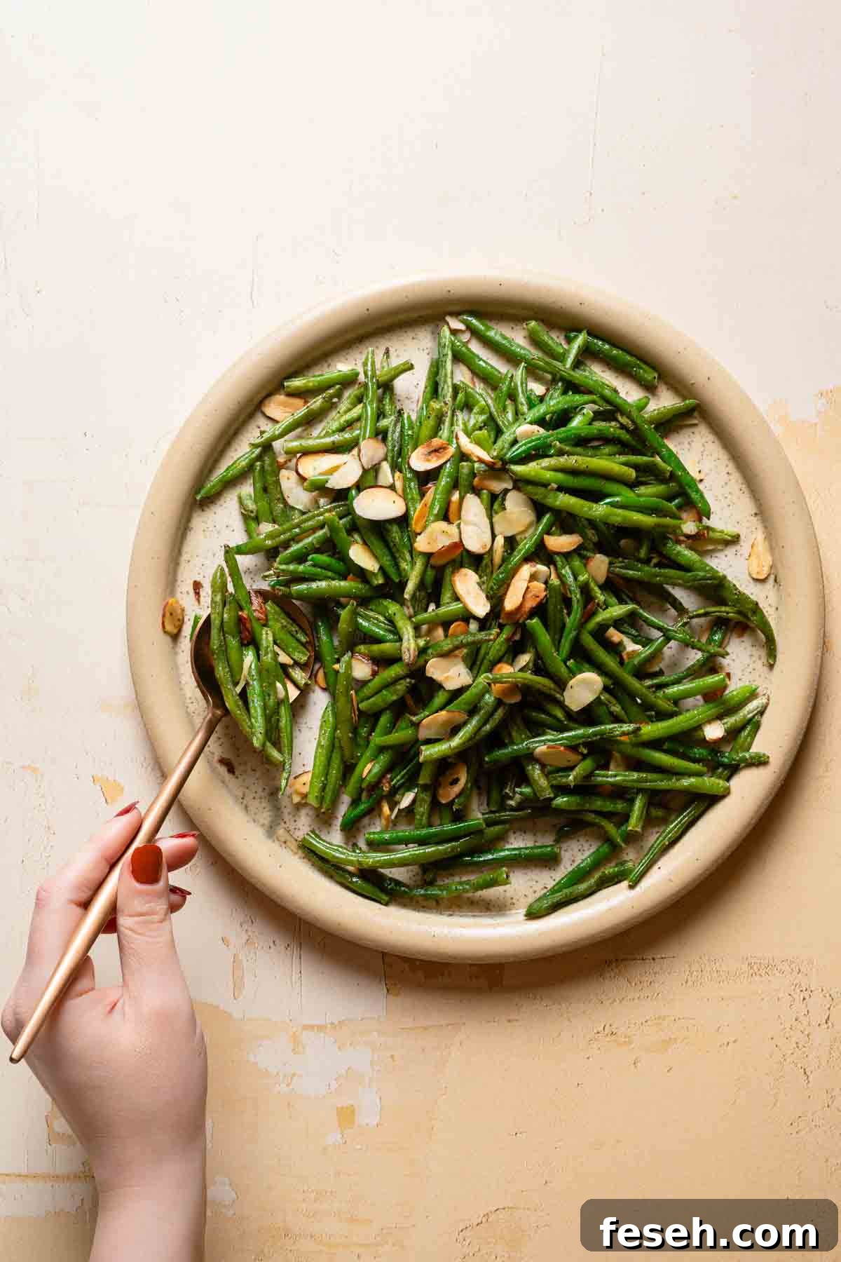 hand serving from plate of cooked green beans and toasted almonds.