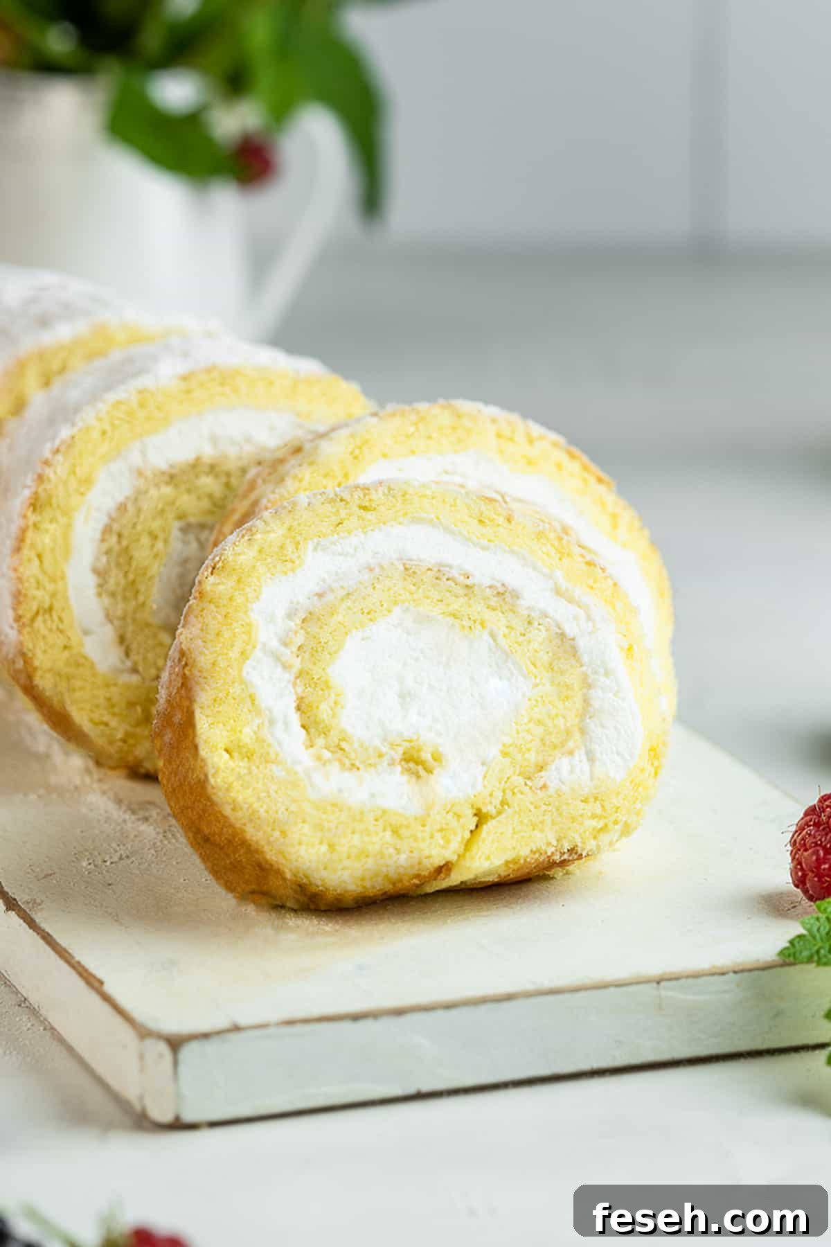 Sliced vanilla sponge cake roll on a serving board.
