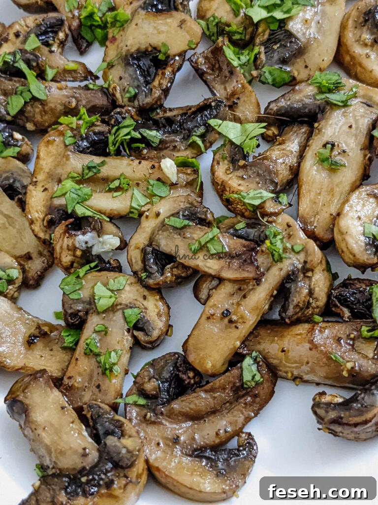 Close up of crispy juicy air fried mushroom slices garnished with cilantro leaves on a white plate.