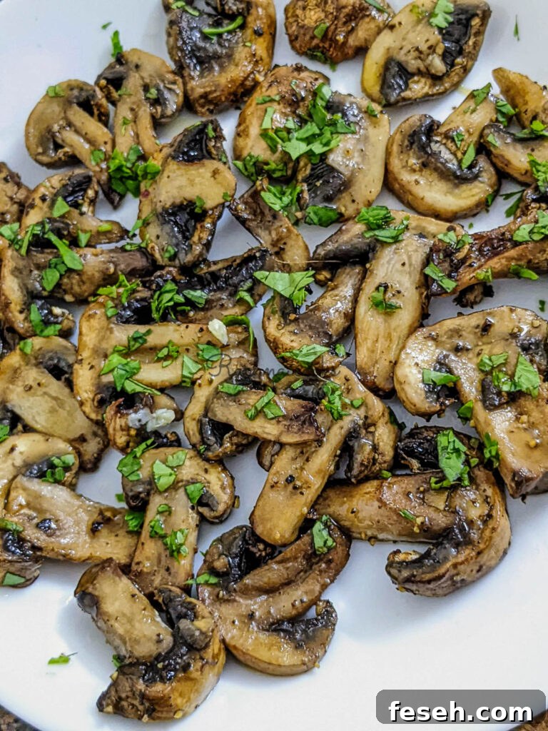 Close up of crispy juicy air fried mushroom slices garnished with cilantro leaves on a white plate.