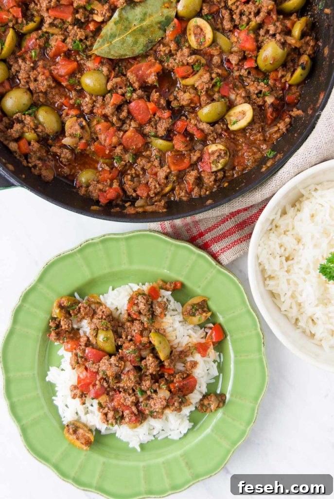 Picadillo is served over rice in a bright green bowl next to a pan holding more picadillo and a bowl holding extra rice