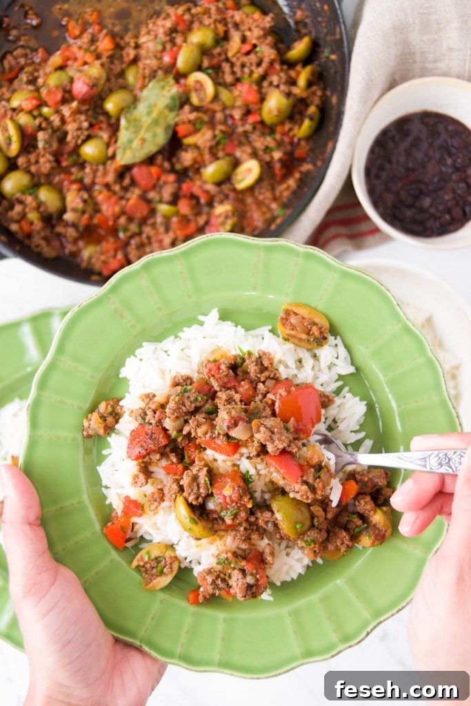 A person holds a utensil in picadillo over rice inside a green bowl