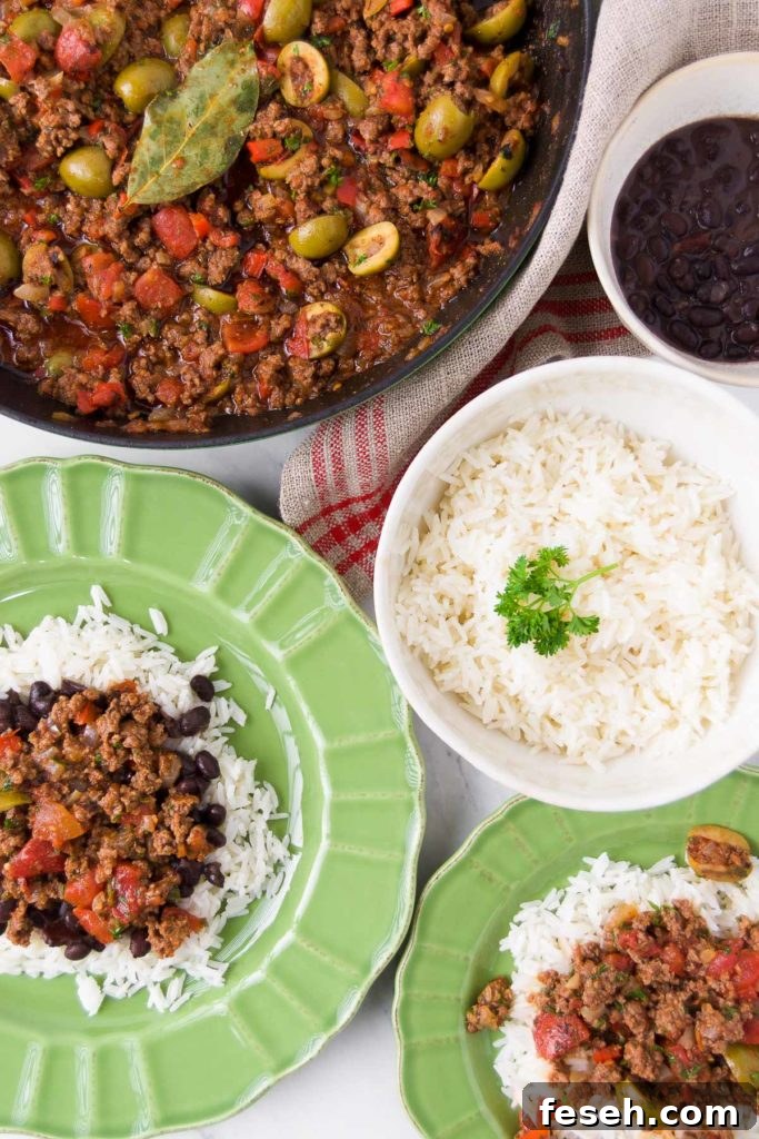 Green bowls hold servings of Brazilian picadillo over rice with beans and sit next to a skillet holding more picadillo and bowls holding rice and beans