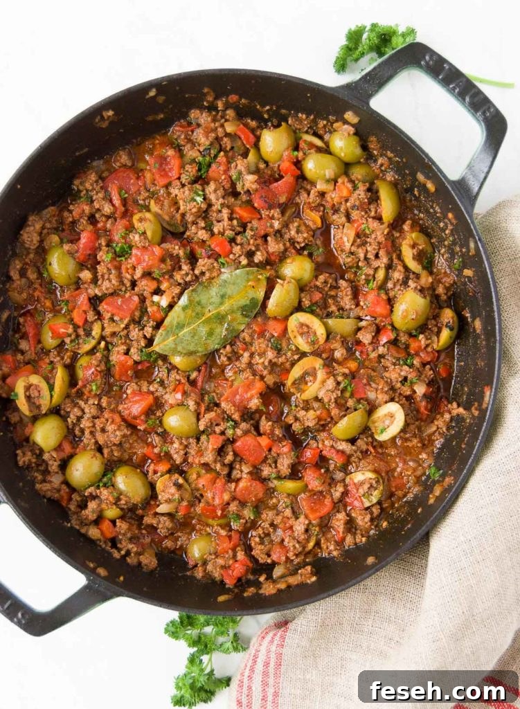 Brazilian Picadillo in a black braising pan sits on top of a red and beige striped towel