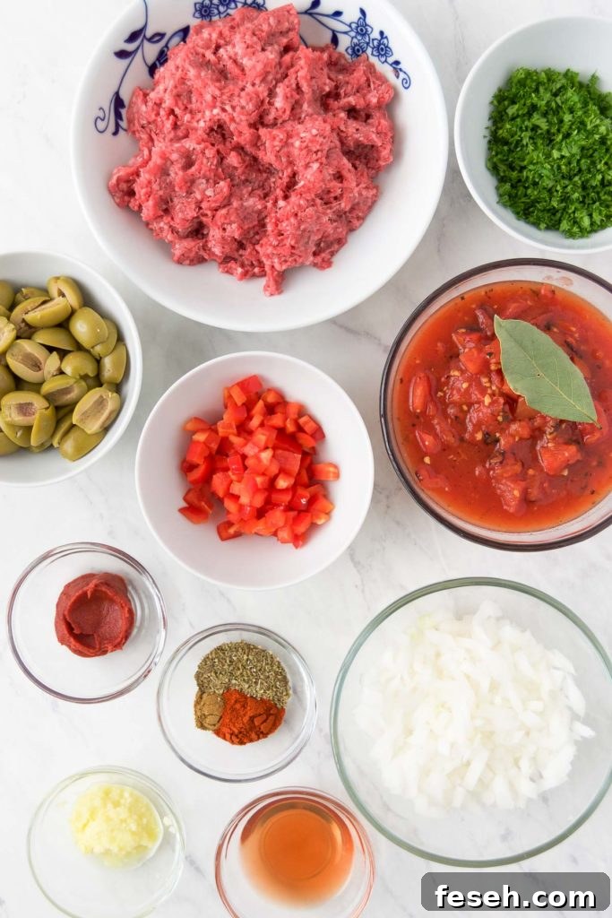 Ground beef, green olives, bell pepper, onion and other picadillo recipe ingredients in bowls from above