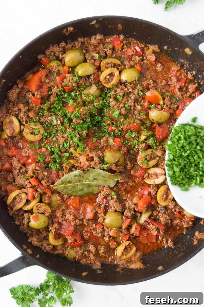 Parsley is sprinkled on top of a Brazilian picadillo recipe in a braising pan from above