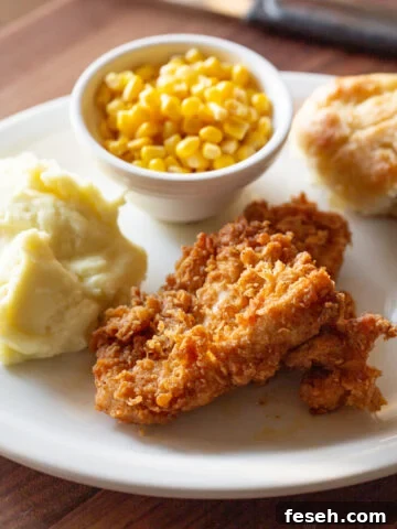 Country fried chicken recipe served with country gravy and a side of mashed potatoes, cranberry sauce, and honey-glazed biscuits