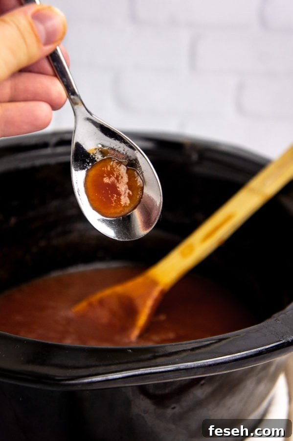 a metal spoon with a dollop of apple butter on it over a crock pot with more apple butter in it