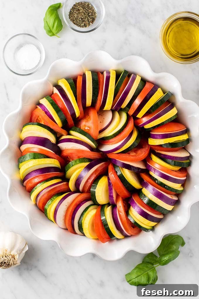 A baking dish shown with layers of tomatoes, eggplant, zucchini, and summer squash.