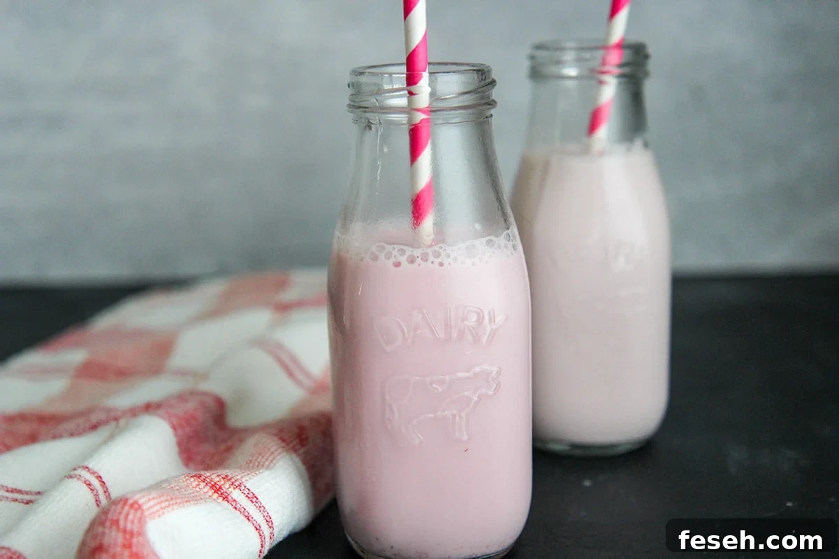 two milk jugs with strawberry milk, straws, and a red and white towel on the side. 