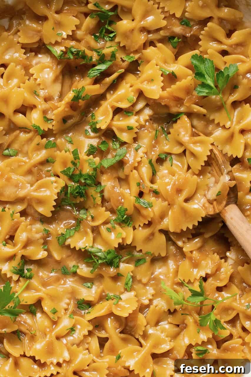an up close photo of cooked french onion pasta being stirred with a wooden spoon. 