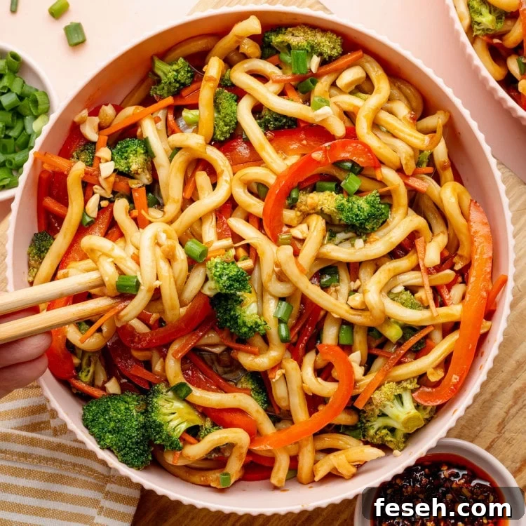 Overhead image of a bowl of sesame udon noodles with broccoli, carrots, and red bell peppers.