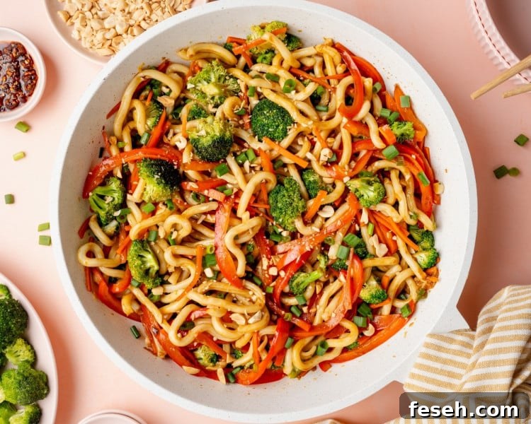 Finished sesame udon noodles tossed together with vegetables, garnished with green onions and chopped peanuts, ready to serve.