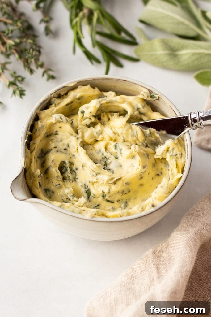 A small bowl with compound herb butter in it, with a butter knife sticking out. The bowl is surrounded by fresh thyme, rosemary, and sage as well as a tan linen napkin.