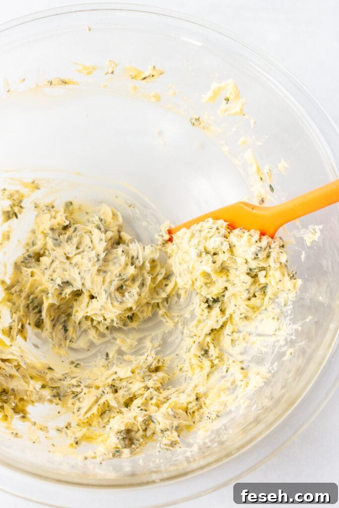 A red spatula scooping out herb butter from a large clear bowl.