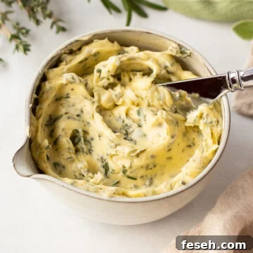 A small bowl with compound herb butter in it, with a butter knife sticking out. The bowl is surrounded by fresh thyme, rosemary, and sage as well as a tan linen napkin.
