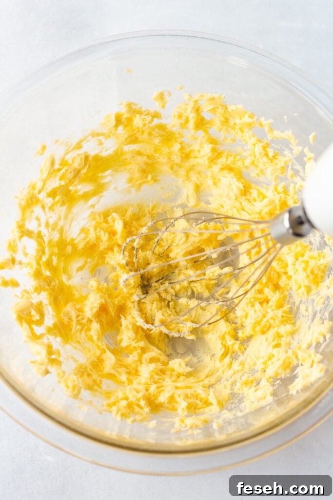An electric beater whipping butter in a large clear bowl.