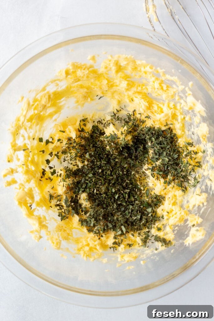 Fresh finely chopped herbs in a large clear bowl with whipped butter in it.