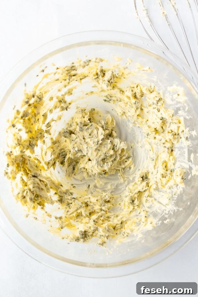 Whipped herb butter in a large clear bowl on a white background.