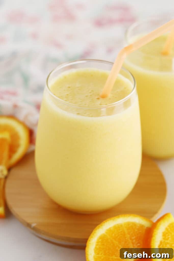 A glass of homemade orange julius with a straw and fresh slices of oranges.
