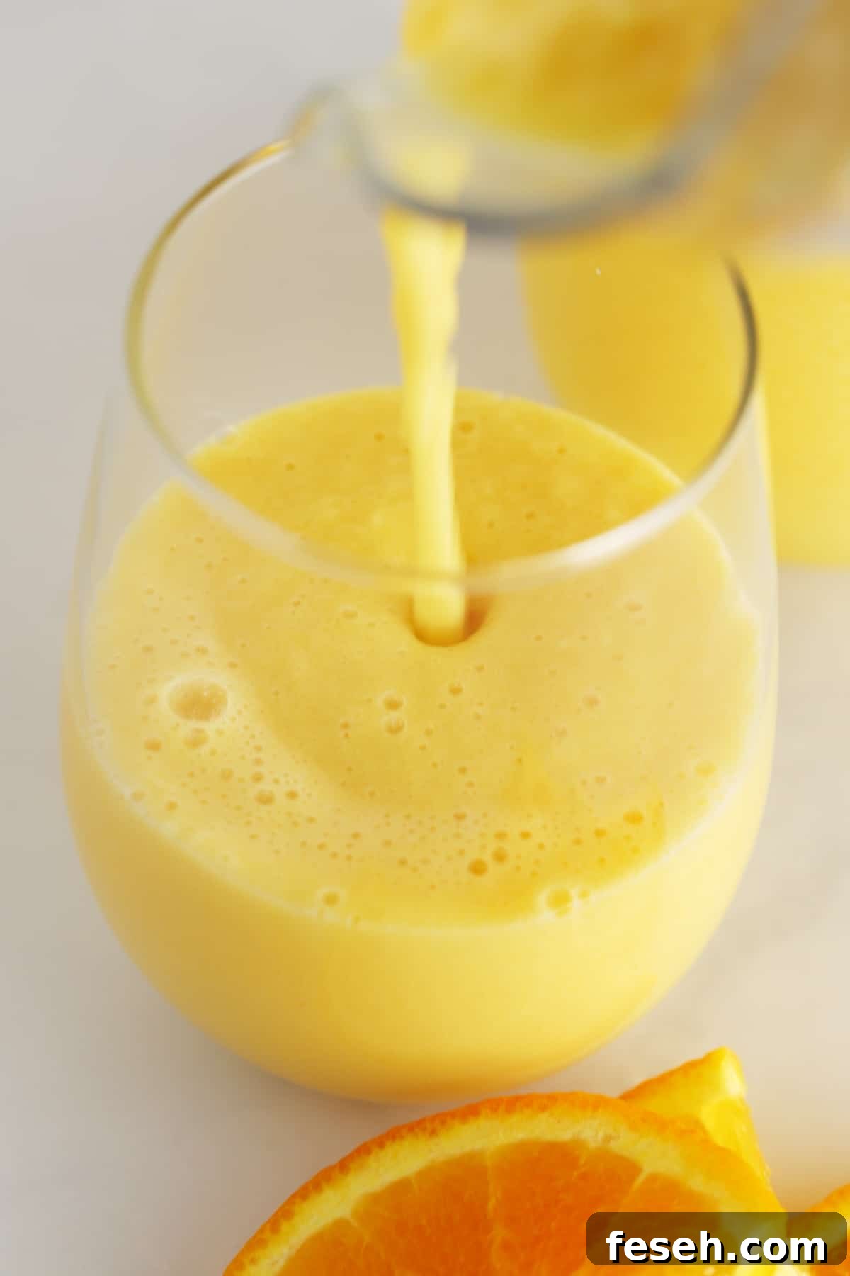 A glass with orange julius being poured into it.