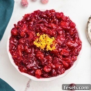 Bright red cranberry sauce in a white bowl, topped with orange zest as a garnish.
