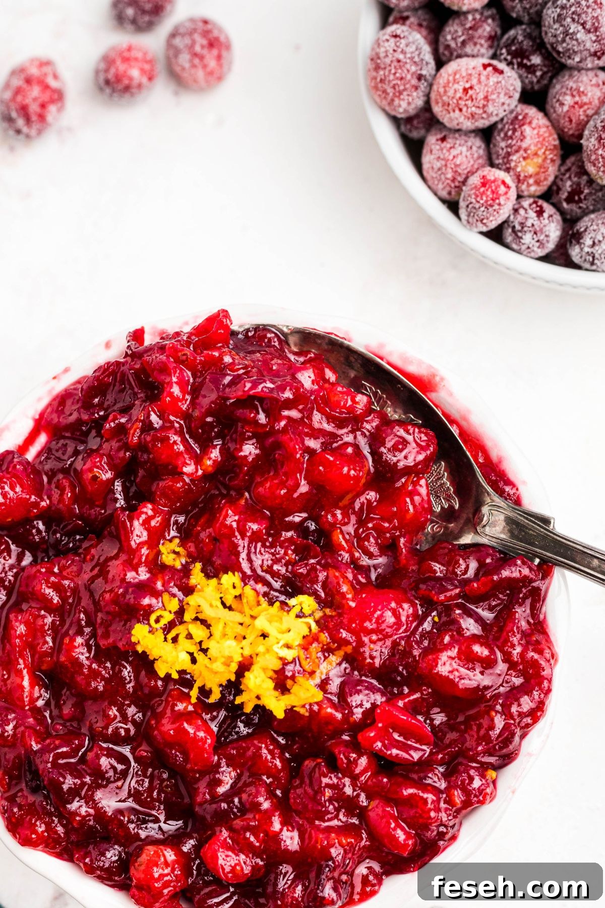 A large silver spoon scooping out cranberry sauce in a white bowl. 