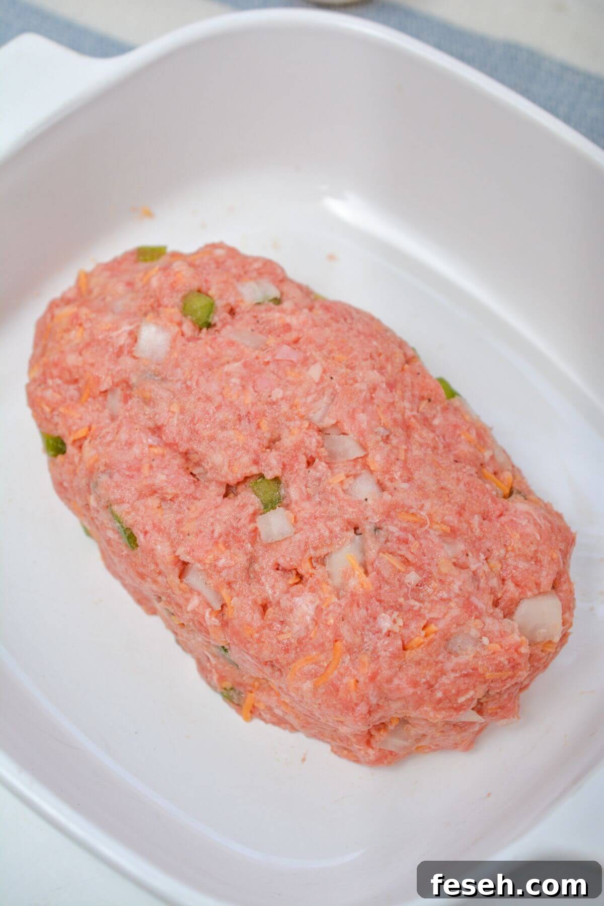 Uncooked meatloaf in a white dish.