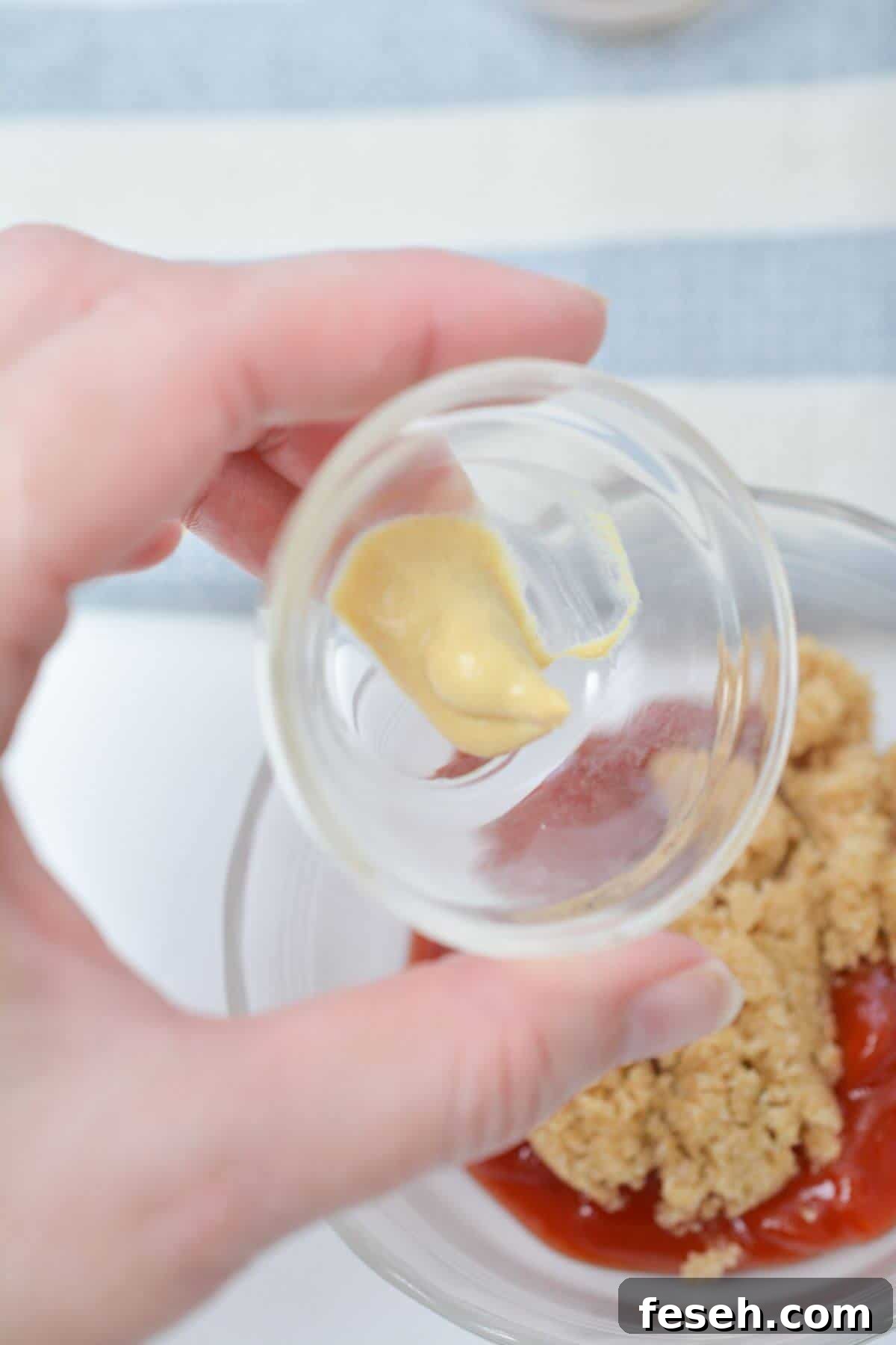 A person is holding a bowl with mustard in it over other sauce ingredients.