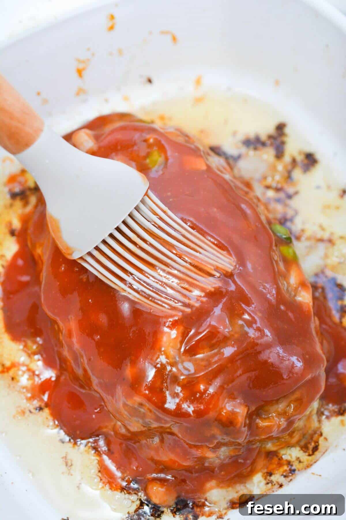 A brush is being used to brush sauce onto meatloaf.