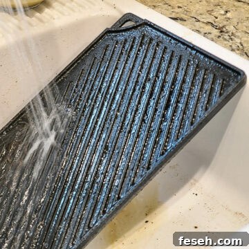 water spraying on cast iron griddle in a sink.