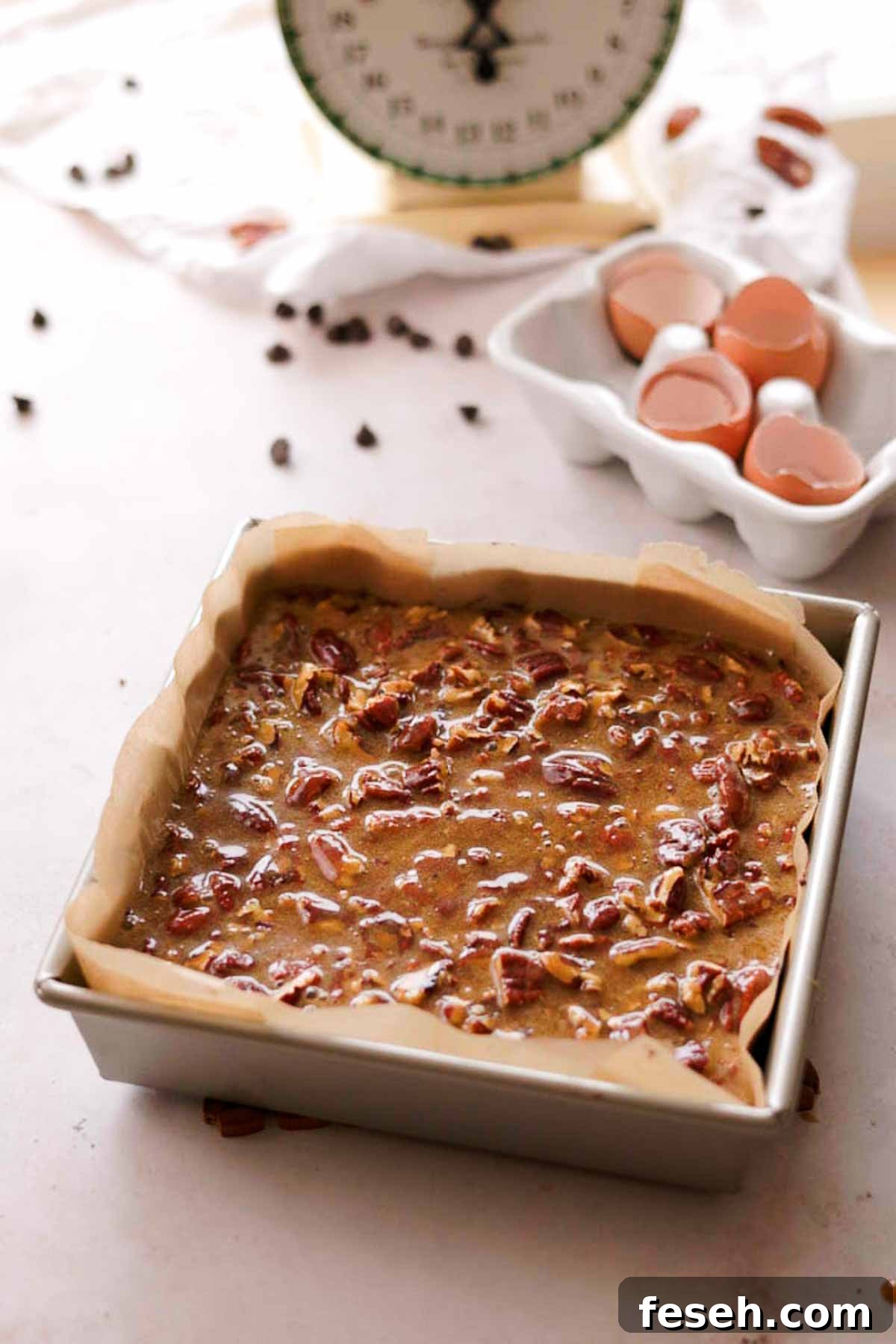 brownie batter in a square tin pan with a layer of pecan butter topping
