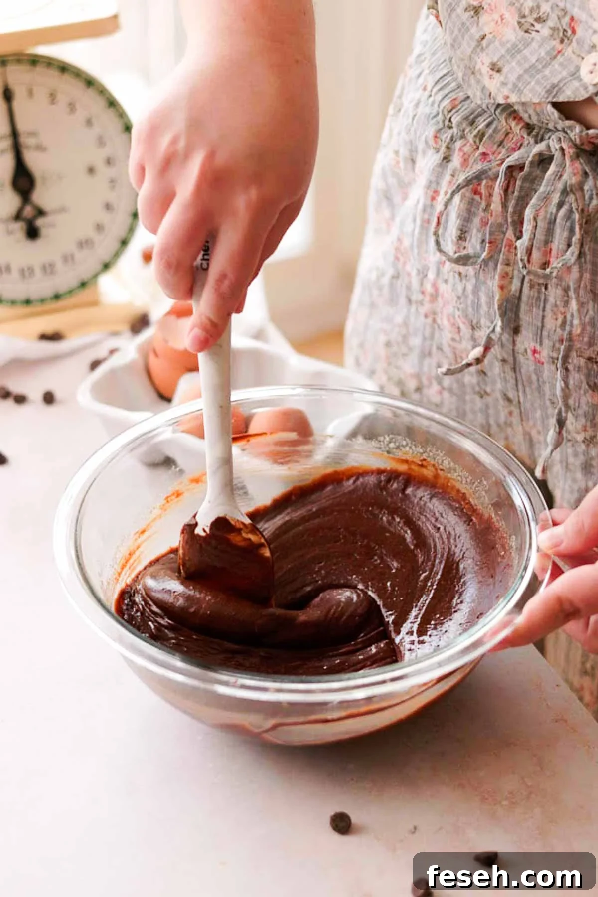 stirring melted chocolate into brownie batter with a spatula in a glass bowl