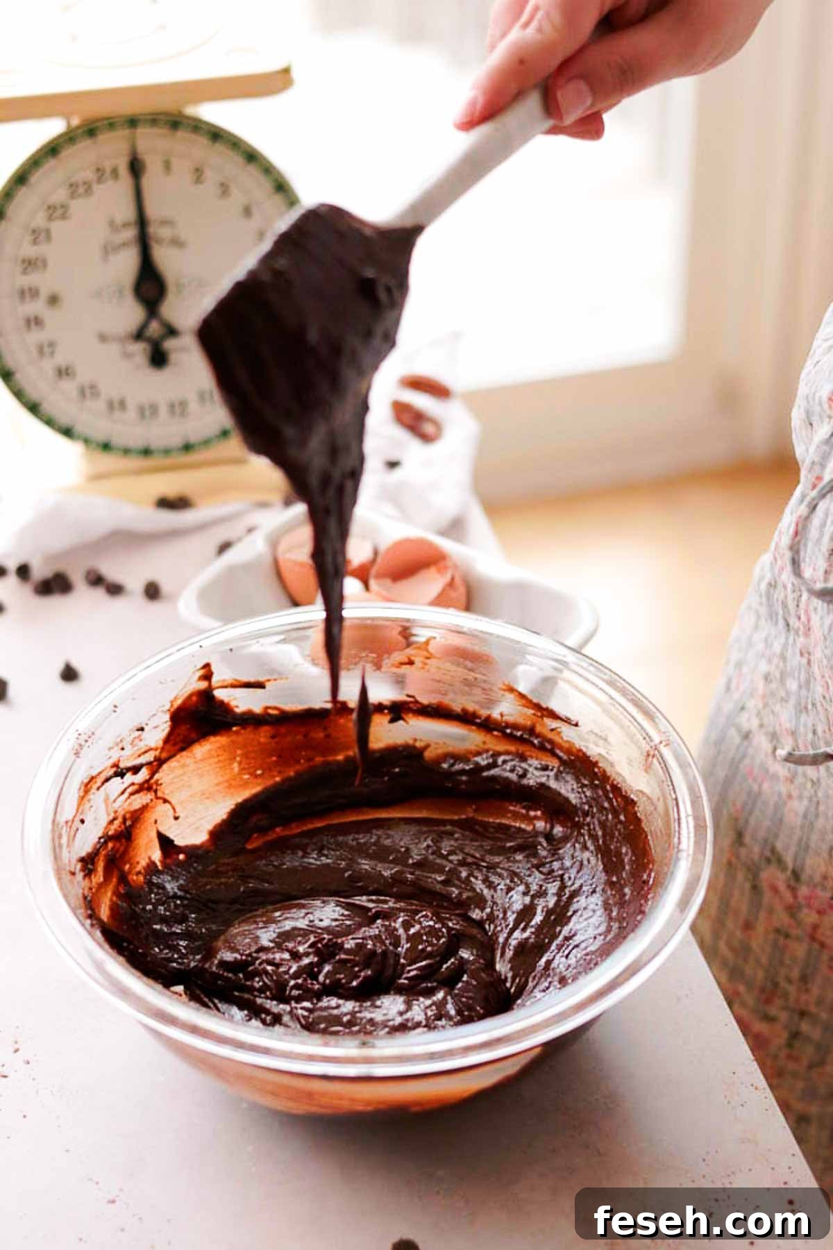 raw brownie batter falling off of a silicone spatula into a bowl of batter