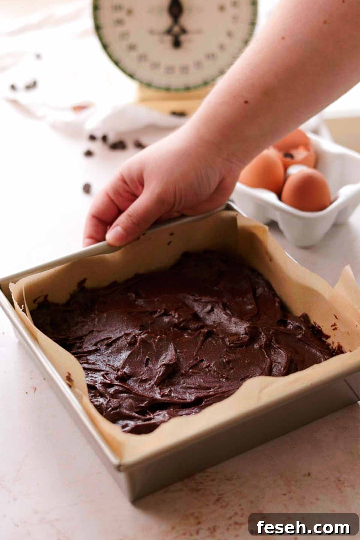 spread brownie batter in a square tin pan with parchment paper